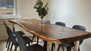 Una mesa rectangular de madera con un florero de vidrio con plantas verdes, rodeada por seis sillas negras.