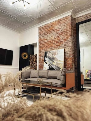 A living room with a brick accent wall, a grey sofa, a coffee table, and a painting.