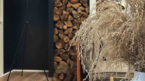 Una habitación con una lámpara de pie moderna, un cuadro en la pared, un conjunto de troncos de madera y un florero con plantas secas.