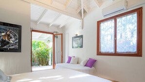 A bedroom with two beds, a large window with a view of greenery, and a ceiling fan. - Villa Secrète, hidden from view and close to beaches and shops (Saint-François)