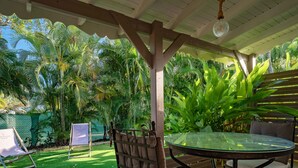 A covered outdoor seating area with a glass table and metal chairs, surrounded by lush greenery and a fenced garden. - Villa Secrète, hidden from view and close to beaches and shops (Saint-François)