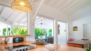 A modern kitchen with a central island, a dining area with a glass table, and a view of lush greenery outside. - Villa Secrète, hidden from view and close to beaches and shops (Saint-François)