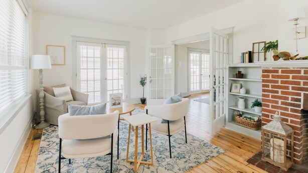 Un salon lumineux, avec des meubles blancs, une cheminée et un plancher en bois.