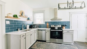 Une cuisine moderne avec des meubles blancs, un pare-feu bleu, des appareils en acier inoxydable et un luminaire suspendu.