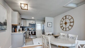 A modern kitchen with white cabinetry, a large clock, and a dining area with white chairs and a round table. - New cozy home near Outlets & Amish Country (Lancaster)