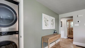 A laundry room with a washing machine and dryer, a wooden bench, and two framed floral artworks on the wall. - New cozy home near Outlets & Amish Country (Lancaster)
