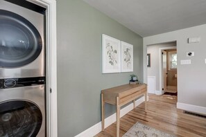 A laundry room with a washing machine and dryer, a wooden bench, and two framed floral artworks on the wall. - New cozy home near Outlets & Amish Country (Lancaster)