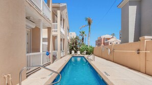 A swimming pool with a view of adjacent buildings and palm trees. - Newly Remodeled 2BR/2B Condo (South Padre Island)