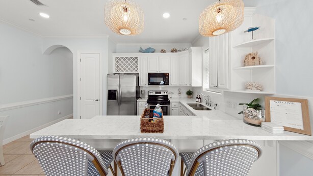 A modern kitchen with white cabinetry, a central island, and three wicker chairs. - Newly Remodeled 2BR/2B Condo (South Padre Island)