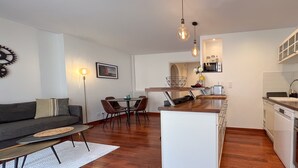 Ett kompakt bostadsutrymme med en soffa, ett matbord, stolar, ett litet kök och en liten köksö.