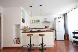 A modern kitchen with a central island, two stools, a microwave, a stove, and a refrigerator. - LE CARNOT Apartment for 2 By Sunset (Antibes)