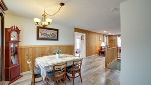 A dining area with a wooden table and chairs, a chandelier, a clock, and a framed picture on the wall.