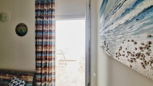 A room with a large abstract painting, a patterned curtain, and a view of the outside. - Appartamento lu Ientu (Porto cesareo)