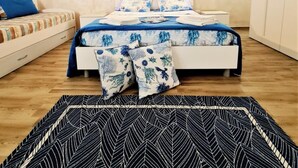 A bedroom with a bed, a nightstand, a bedside table, a wall-mounted painting, and a patterned rug. - Appartamento lu Ientu (Porto cesareo)