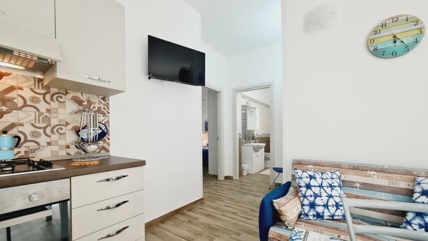 A modern kitchen with white cabinets, a built-in stove, and a flat-screen TV mounted on the wall. - Appartamento lu Ientu (Porto cesareo)