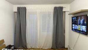 A living room with a TV mounted on the wall displaying a program about suits. - Quartier de Meyrin (Meyrin)