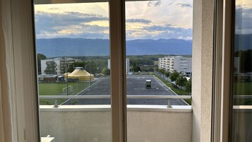 Vista desde una ventana que da a un estacionamiento, una carpa amarilla y edificios a lo lejos, con montañas al fondo.