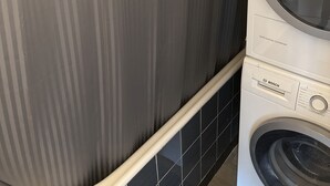 A front-loading Bosch washing machine and dryer stacked in a laundry room with striped wallpaper and black tiled flooring. - Quartier de Meyrin (Meyrin)