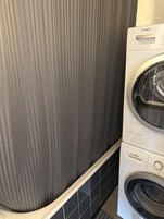 Lavadora y secadora Bosch de carga frontal apiladas en un cuarto de lavado con papel tapiz a rayas y piso de baldosas negras.