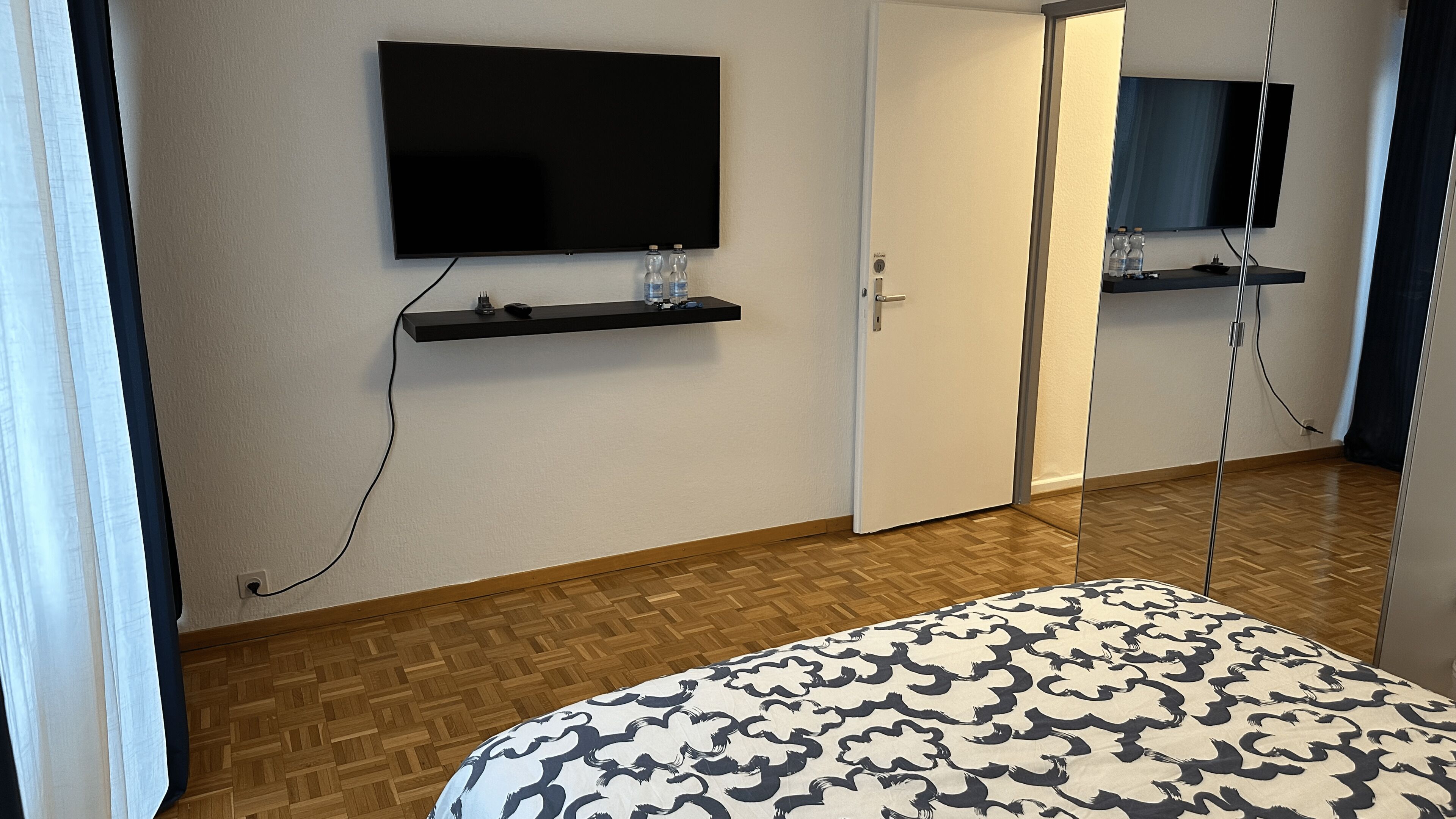 Ett hotellrum med en säng, en tv som är monterad på väggen och en dörr som leder till ett annat rum.