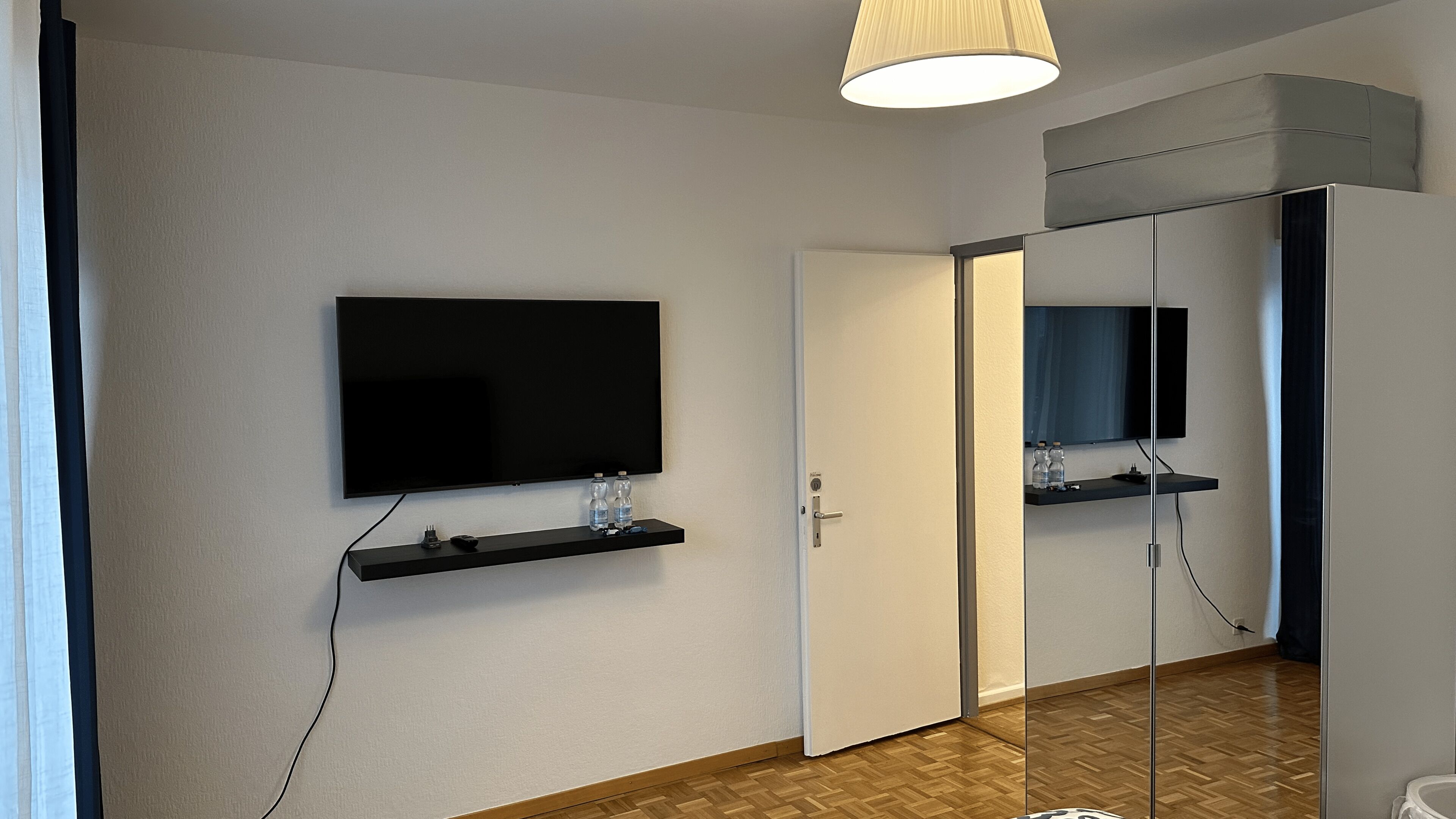 Ein Hotelzimmer mit Flachbildfernseher an der Wand, einer Tür und einem Spiegel.