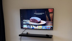A television mounted on a wall with a shelf below it. - Quartier de Meyrin (Meyrin)