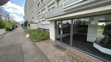 Un edificio moderno con entrada de vidrio, número 35, un área pavimentada con motocicletas estacionadas y un pequeño jardín.