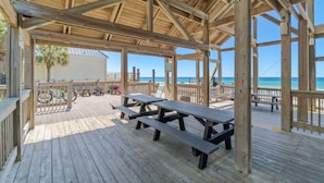 Een houten terras met picknicktafels, met uitzicht op een strand en de oceaan.