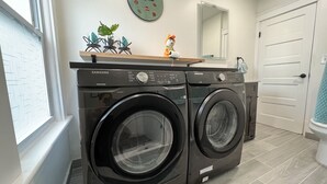 A laundry area with two black Samsung washing machines, a decorative clock, and a small plant on a shelf. - Trendy in Tremont, Cleveland U (Cleveland)