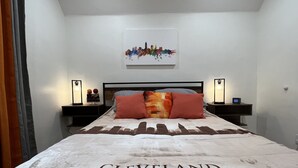 A hotel room with a bed featuring a printed cityscape, two bedside tables with lamps, and a framed picture on the wall. - Trendy in Tremont, Cleveland U (Cleveland)