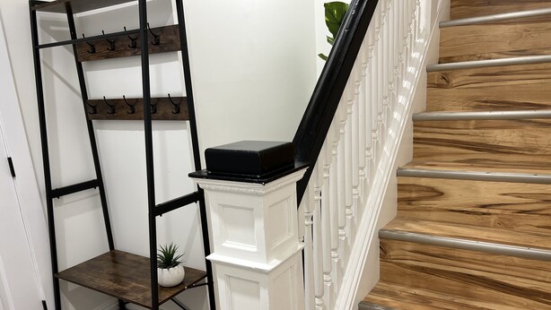 A staircase with wooden steps and a white balustrade, a black metal shelf unit with hooks, and a small potted plant. - Trendy in Tremont, Cleveland U (Cleveland)