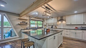 Cocina moderna con una isla grande, armarios blancos y una viga de techo de madera.