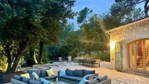 An outdoor patio area with wicker furniture, stone flooring, and a stone building with large windows. - Charming Estate on 1Ha: 3 Houses, Heated 28 °C Pool, SPA, Ideal for Families (Roquefort les pins)