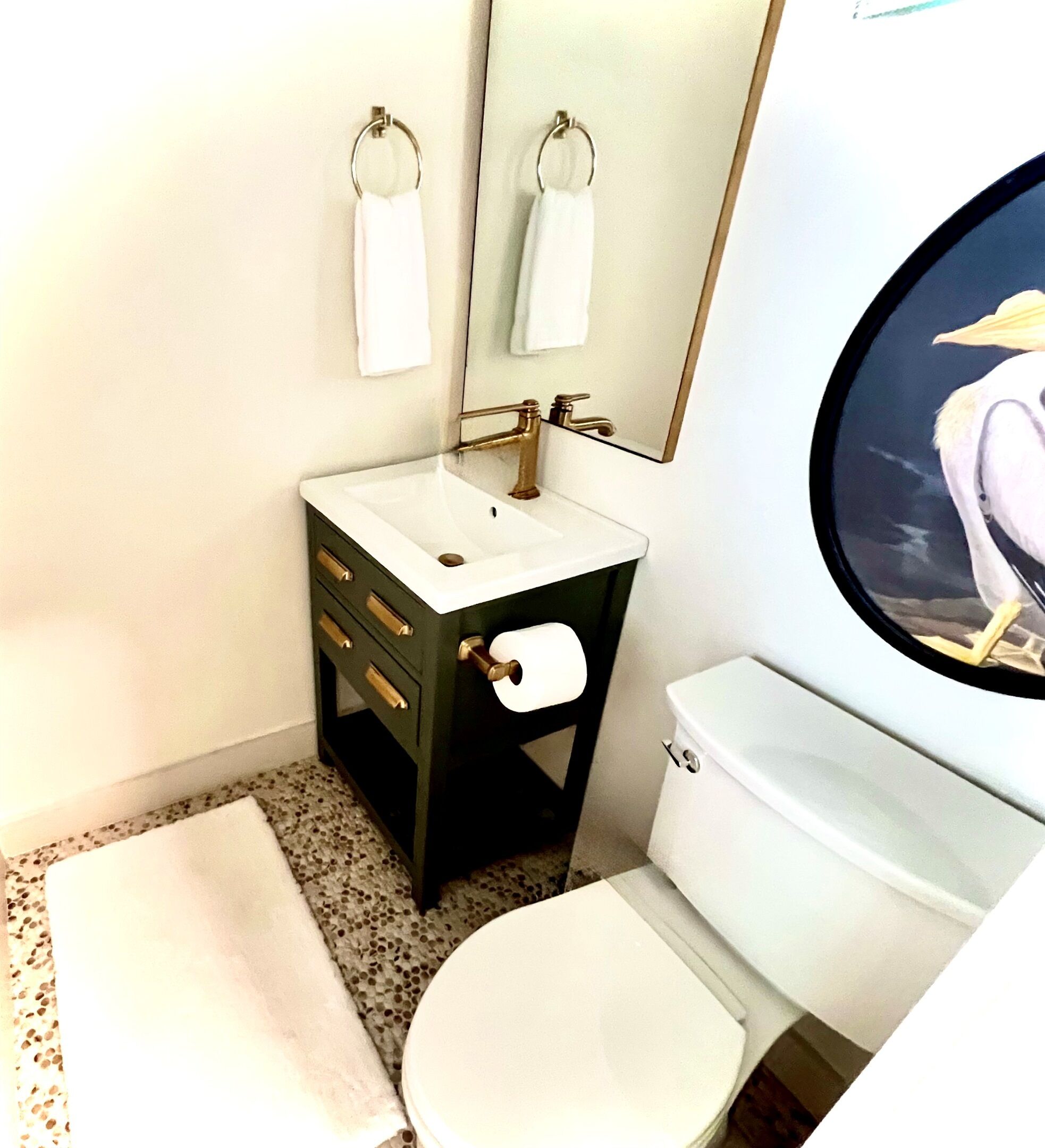Et badeværelse med et hvidt håndvask, toilet, spejl og et håndklædestativ.