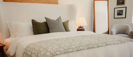 A hotel room with a bed, a nightstand, a lamp, a chair, and a mirror.