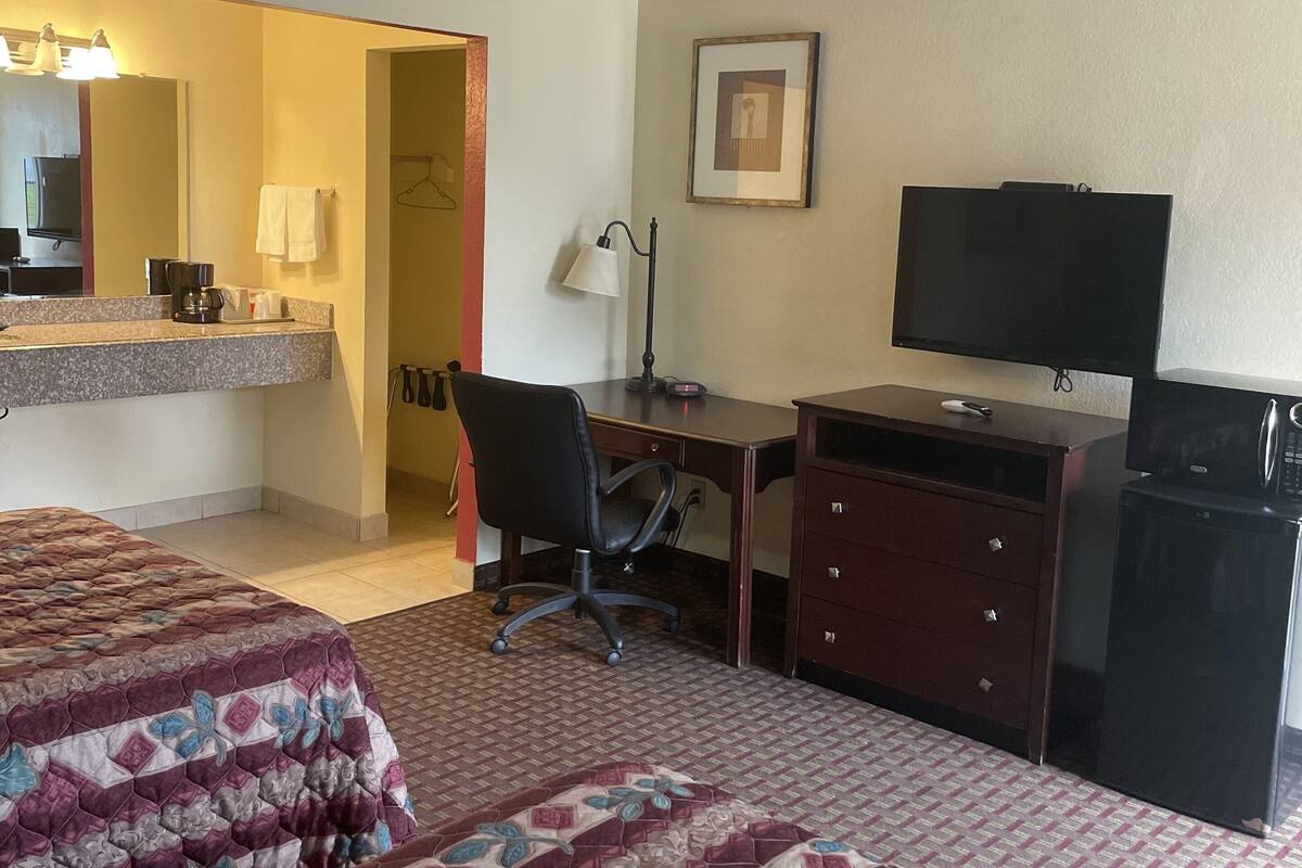 A hotel room with two beds, a desk, a chair, a television, a dresser, and a mirror.