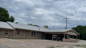 A building with a sign reading "OFFICE" on the front, a covered parking area, and a clear sky. - Village Inn (Ada)