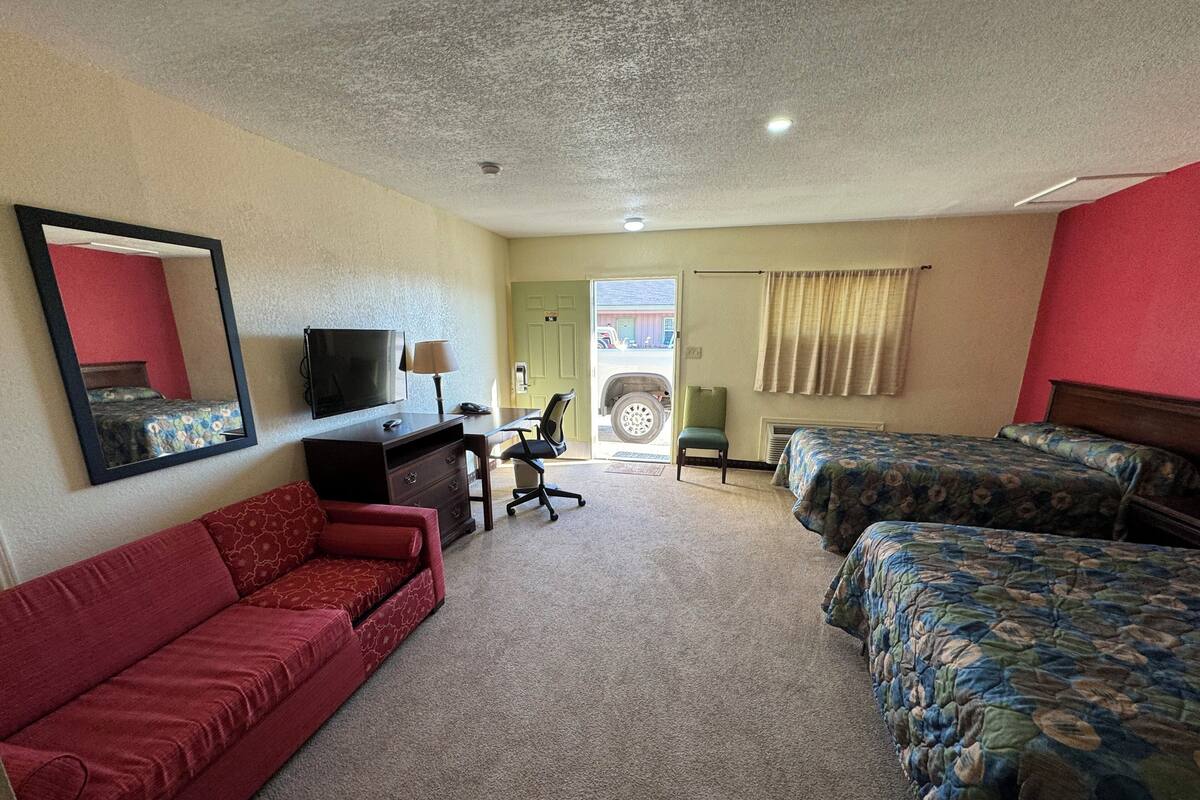 A hotel room with a red sofa, two single beds, a desk with a chair, a television, and a mirror.