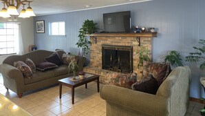 A living room with a fireplace, a sofa, a coffee table, and a television. - Village Inn (Ada)