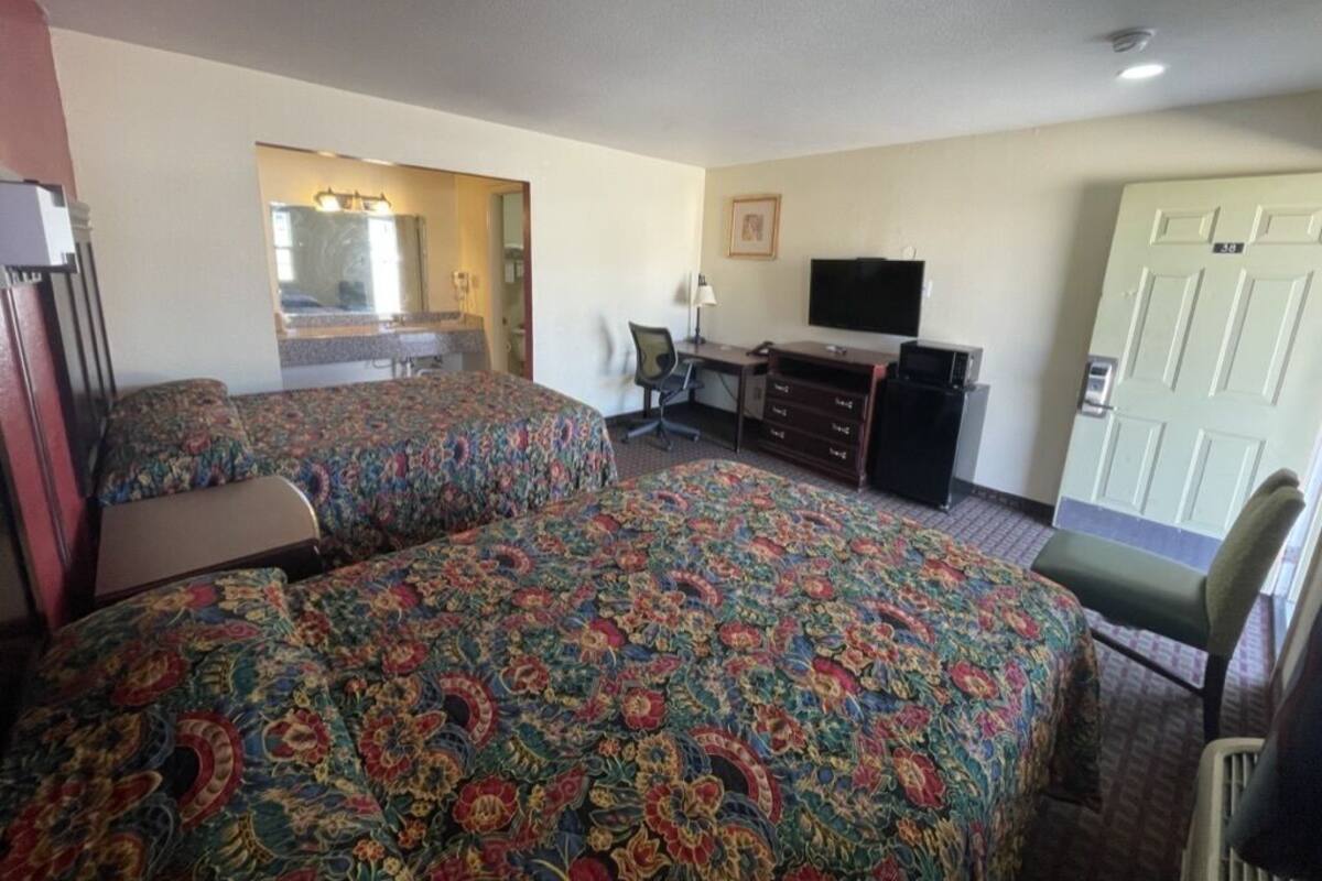 A hotel room with two beds, a desk, a chair, a television, and a door.