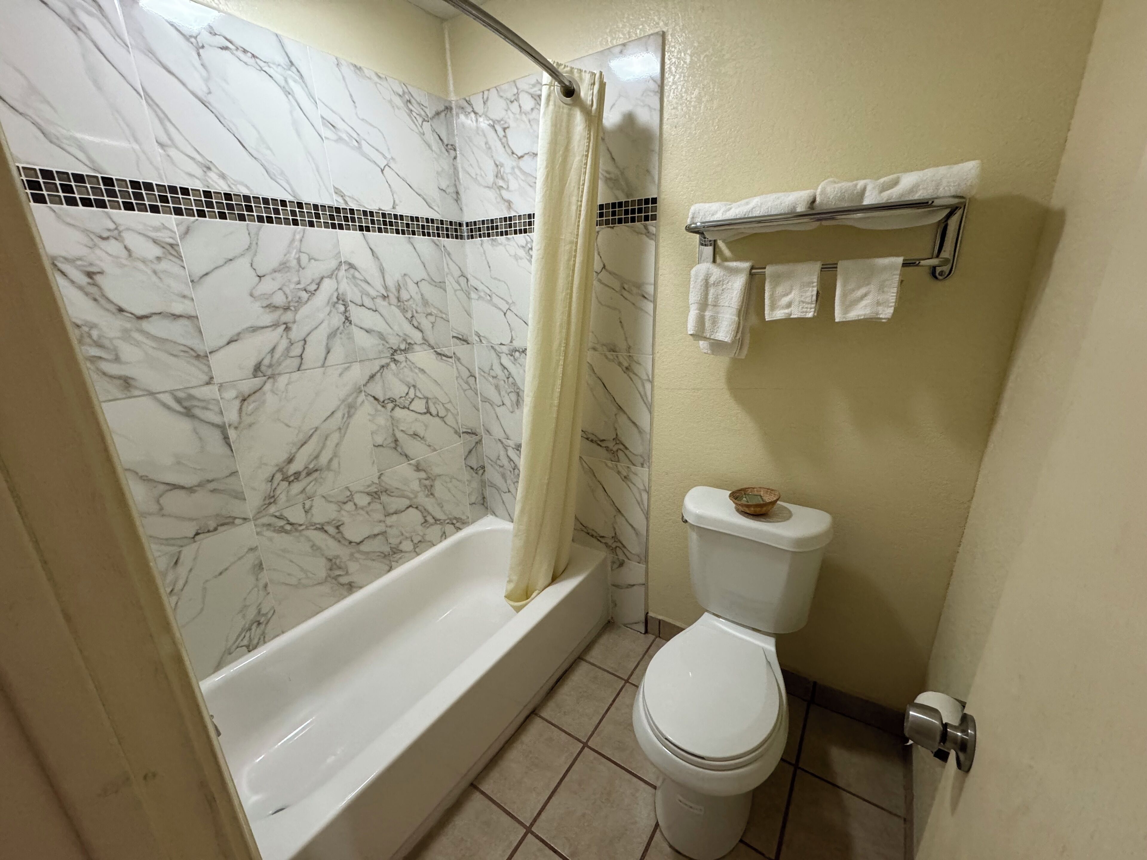 Un baño con pared de ducha de mármol, bañera, inodoro y toallero con toallas.