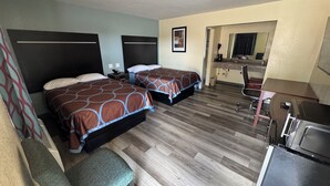 A hotel room with two beds, a desk, a chair, a kitchenette, and a bathroom visible through an open doorway. - Village Inn (Ada)