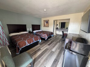 A hotel room with two beds, a desk, a chair, a refrigerator, and a bathroom visible through an open door.