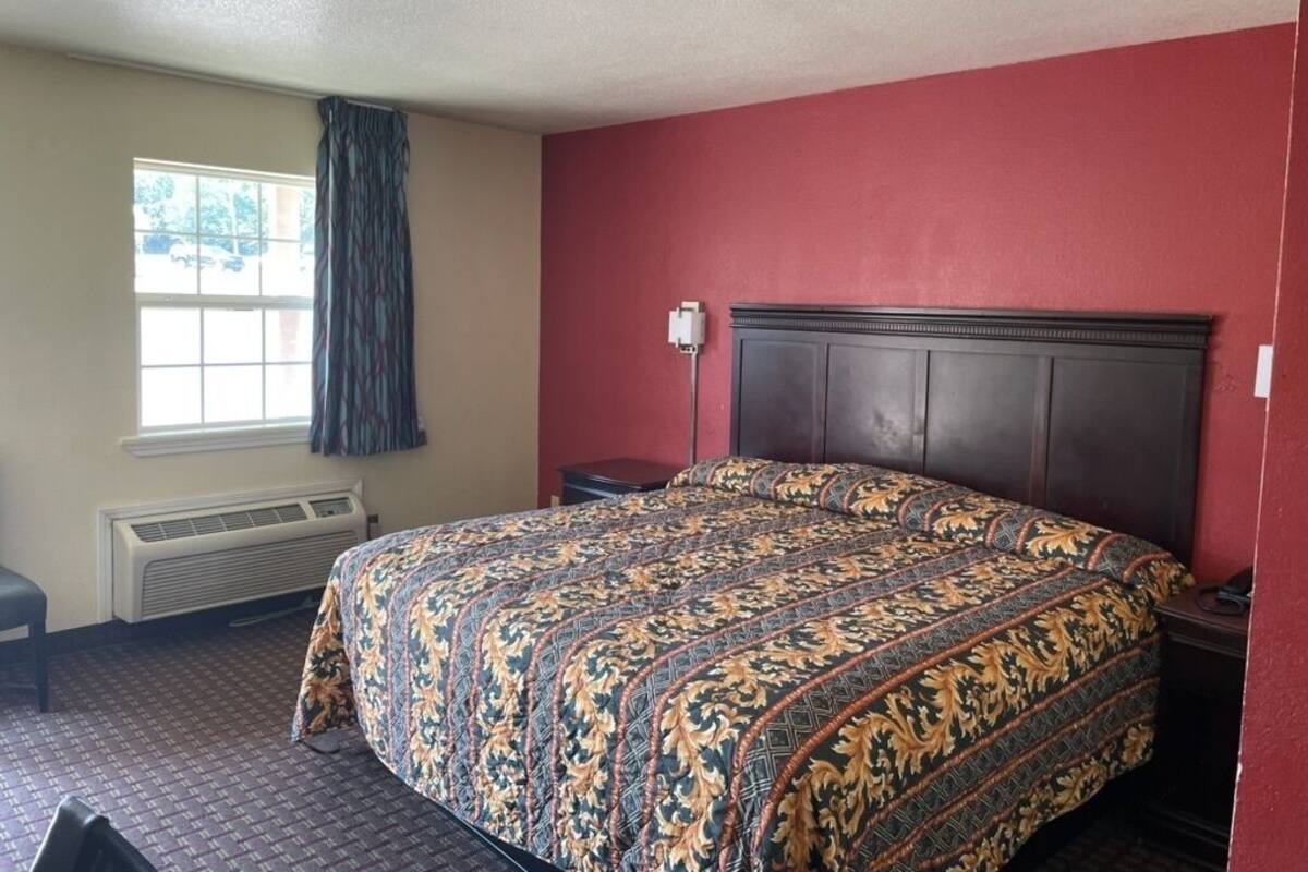 A hotel room with a large bed, a window with curtains, a heater, and a small table.