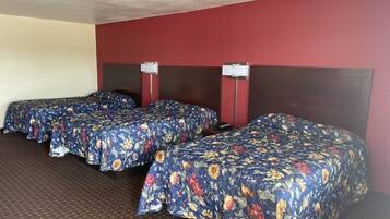 Een hotelkamer met drie eenpersoonsbedden, elk met een bloemenprint deken, een donker hoofdeinde en een nachtkastje met een lamp.