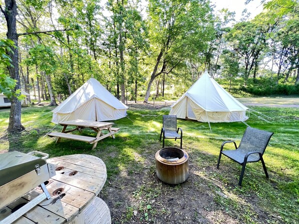 Un camping con dos tiendas de campaña, una mesa de picnic, una parrilla y una fogata.