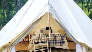 Ein Zelt mit einem Bett, einem Schaukelstuhl und einer karierten Decke darin.