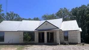 A two-story house with a stone facade, large windows, and a metal roof. - Ranch House (Alba)