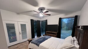 A bedroom with a bed, a ceiling fan, a TV, and a sliding glass door leading to a balcony. - Ranch House (Alba)