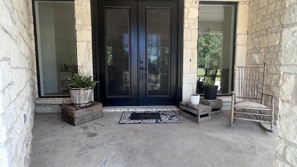 A stone-walled entrance with a dark door, a doormat, and a wooden rocking chair. - Ranch House (Alba)